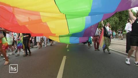 Regenbogefahne von unten links und rechts von Leuten gehalten