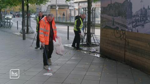 Drei Männer mit Warnwesten sammeln Müll auf