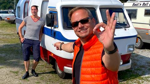 Friso Richter mit Sonnenbrille zeigt auf einen Schwimmcaravan.