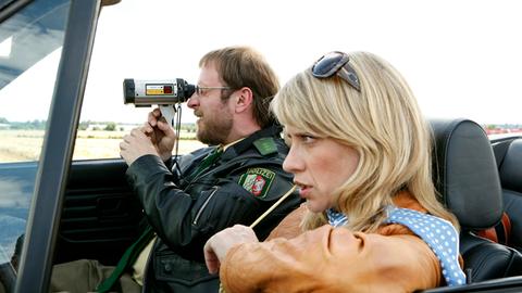 Dietmar Schäffer (Bjarne Mädel, l.) macht begeistert Radarkontrollen am Ortseingang von Hengasch, Sophie Haas (Caroline Peters, r.) ödet die sinnlose Aktion an.