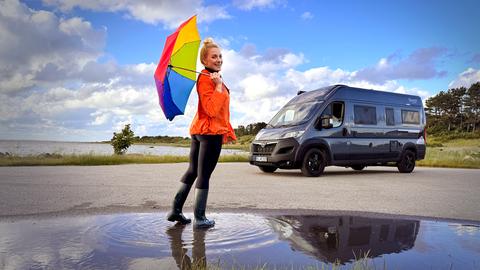 Maike Tschorn mit buntem Regenschirm vor ihrem Campervan im dänischen Seeland.
