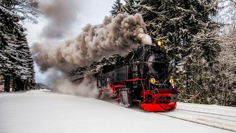 Historischer Zug fährt durch einen verschneiten Wald.