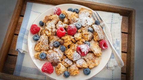 Kaiserschmarrn mit Himbeeren und Blaubeeren auf einem Teller angerichtet.