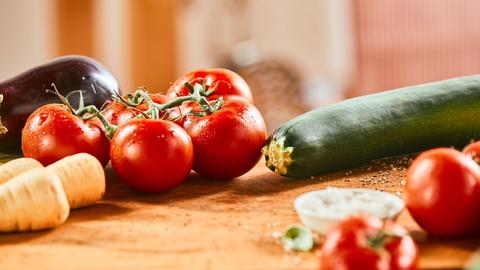 Eine Zucchini und ein Tomatentstrauch liegen auf einer Holzunterlage.