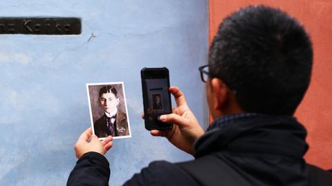 Ein Mann fotografiert mit dem Handy das Haus von Franz Kafka und hält dabei ein Bild von Kafka, das mit auf das Foto soll.