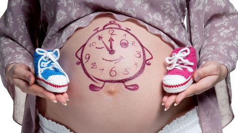 Frau mit Babybauch, auf dem eine Uhr aufgezeichnet ist