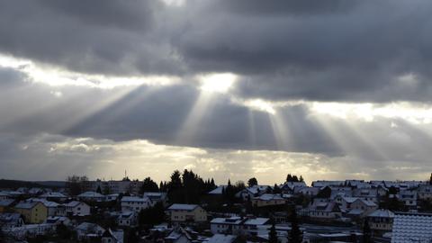 Sonnenlicht bricht durch die Wolken auf ein verschneites Dorf. 