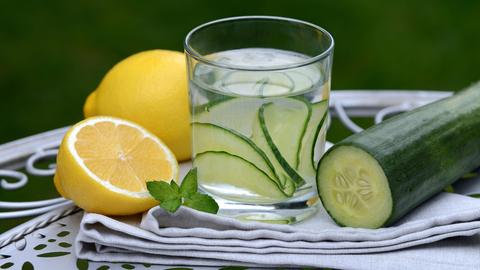 Ein Glas Wasser mit Gurkenscheiben und Zitrone auf einem schnörkeligen Tablett angeordnet.