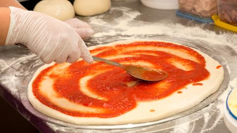 Eine Person bestreicht Pizzateig mit Tomatensoße.