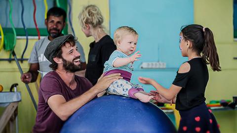 Mann mit Mütze hält Kind auf blauem Ball