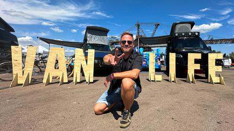 Camping-Fan Friso Richter posiert vor zwei Campern auf Deutschlands größtem Vanlife-Event "Ferropolis" in Gräfenhainichen (Sachsen-Anhalt).