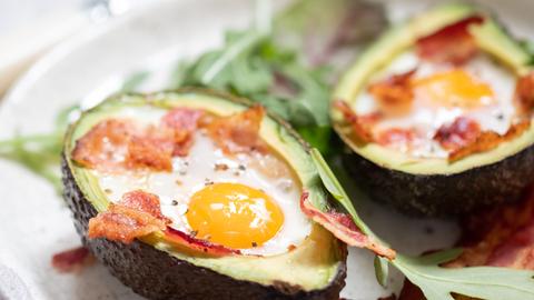 Die Hälfte einer überbackenen Avocado mit Ei und Speck.