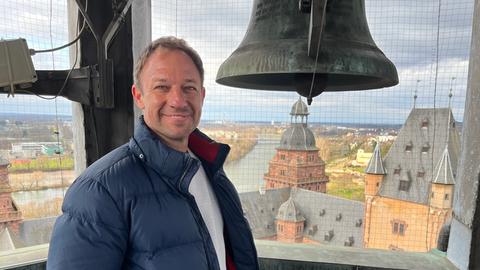 Tobi Kämmerer steht in einem Glockenturm neben einer Kirchenglocke